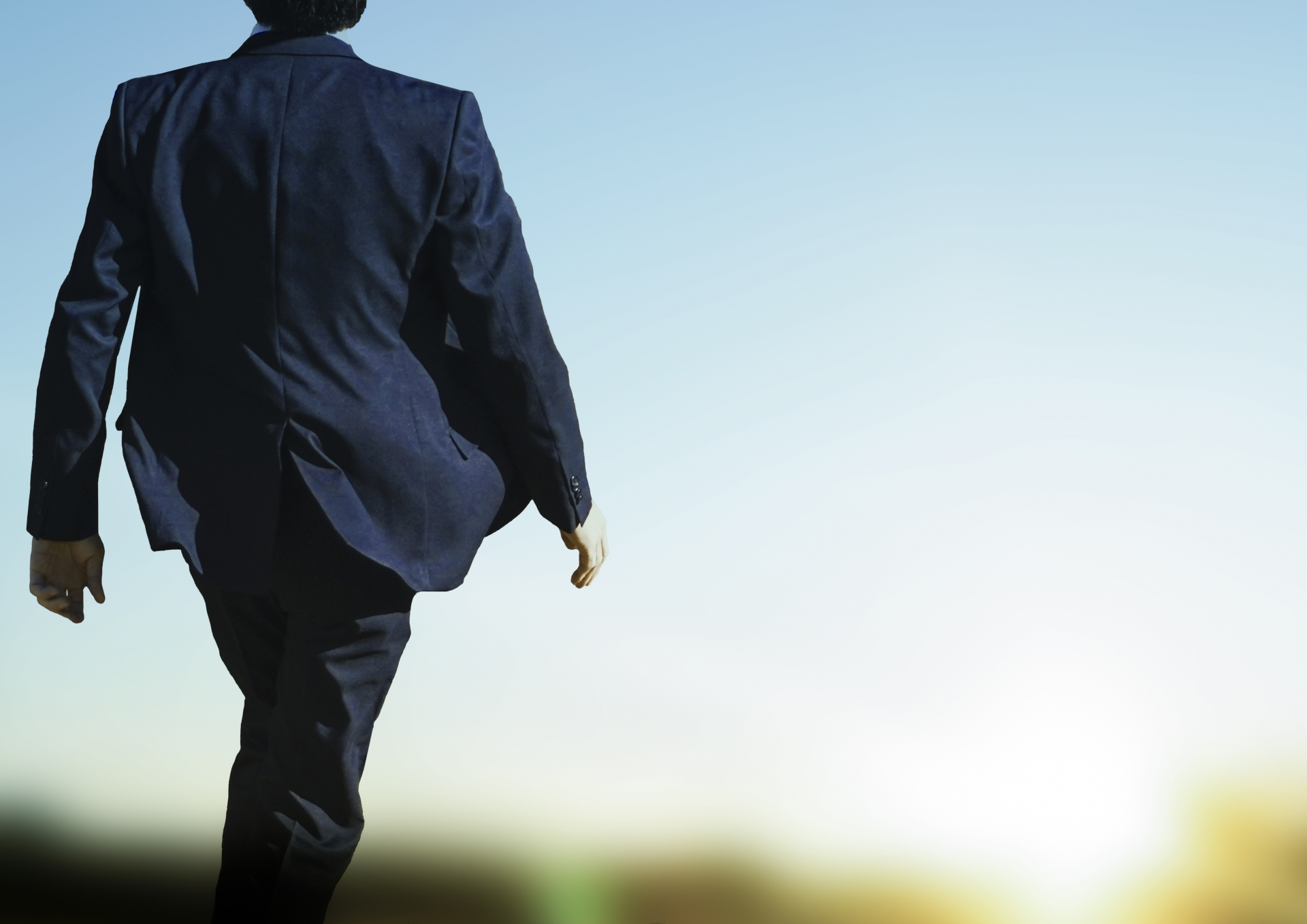 太陽に向かって颯爽と歩くスーツの男性